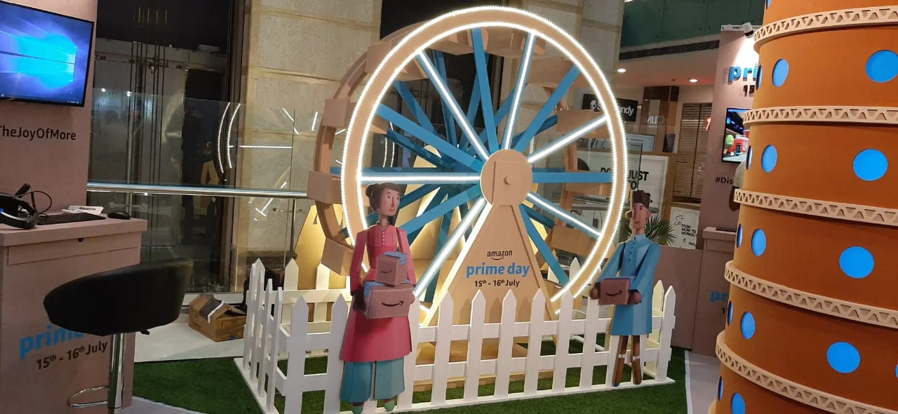 Cardboard ferris wheel with parcel-carrying figures and neon ring at the Prime Day zone