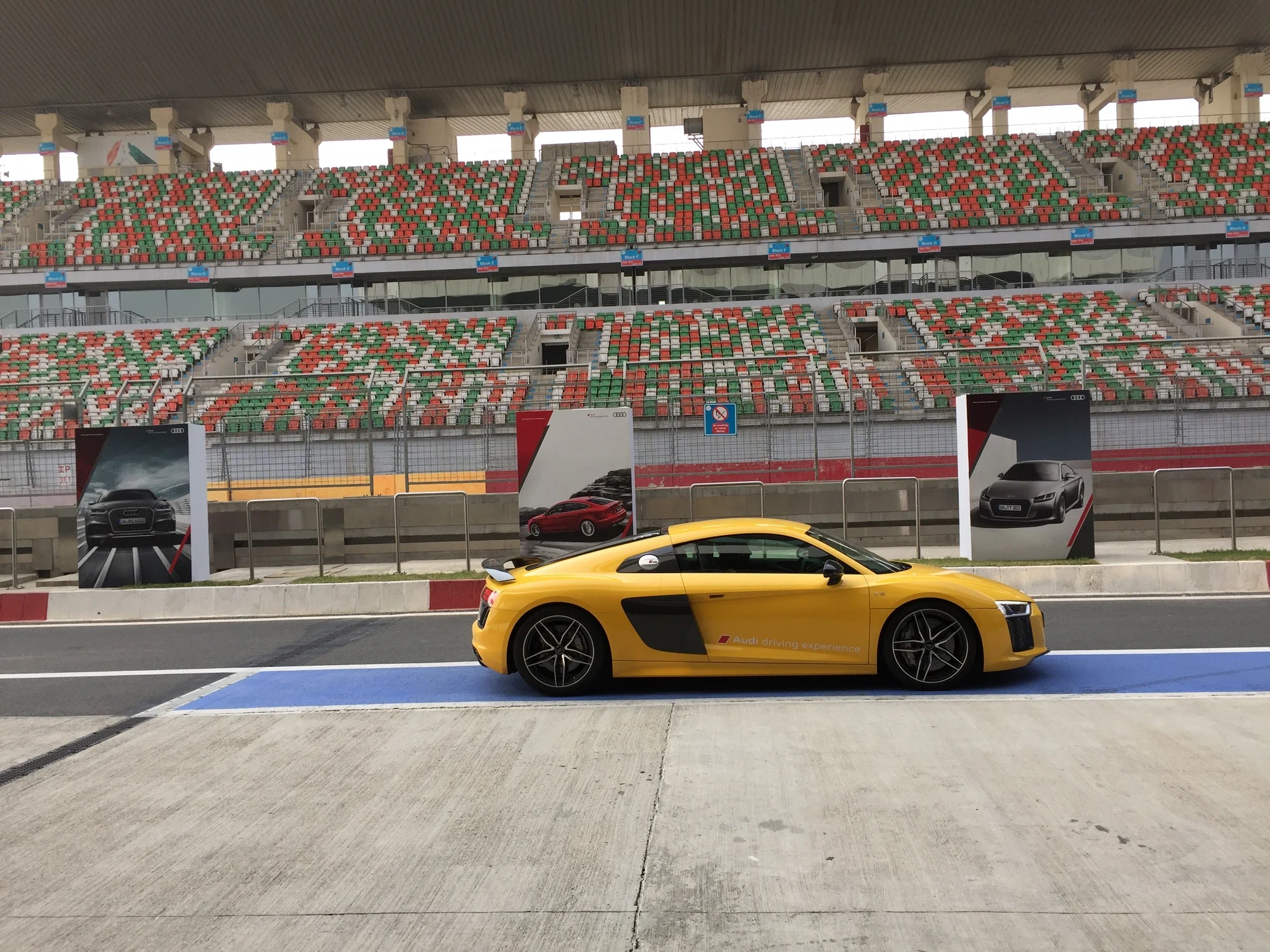 Yellow Audi R8 parked on the Buddh International Circuit pit lane beside branded poster pillars