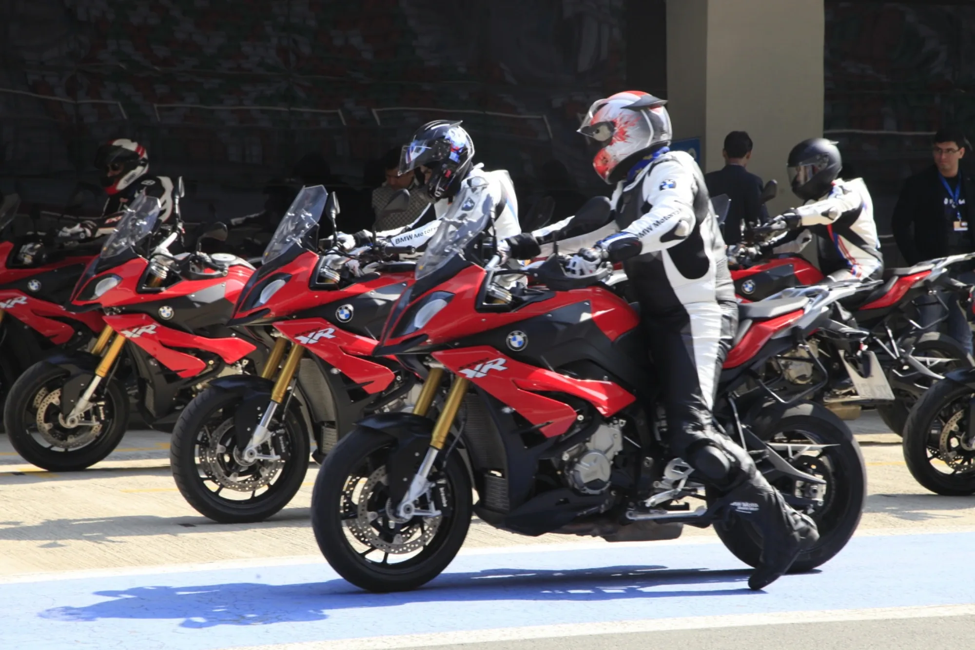 Riders in leathers and helmets lined up on red BMW S 1000 XR motorcycles