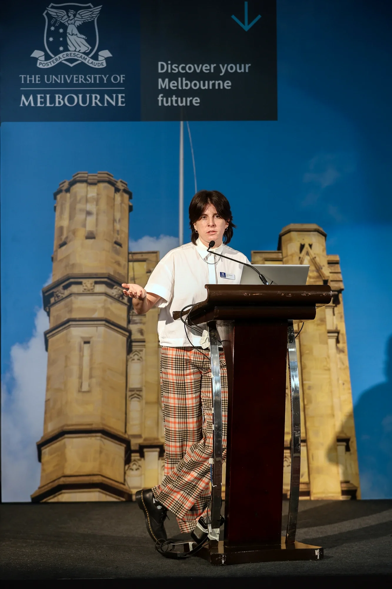 Speaker at the podium against the University of Melbourne campus backdrop