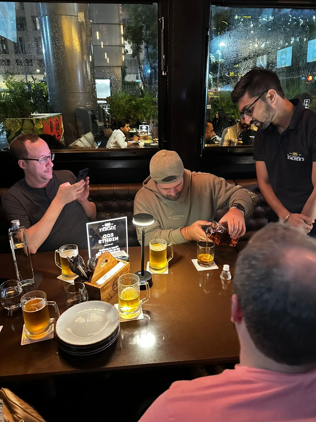 Guests pouring and enjoying Teacher's at a resto-bar table on a rainy evening