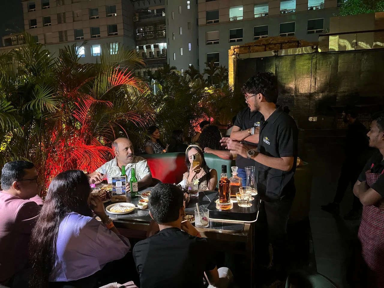 Rooftop EOD Night — host engaging a table of guests over Teacher's serves