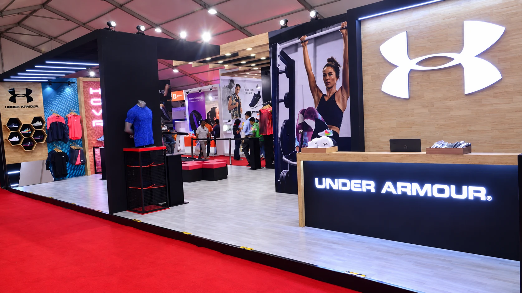 Wide panorama of the Under Armour expo booth with reception desk and illuminated logo wall