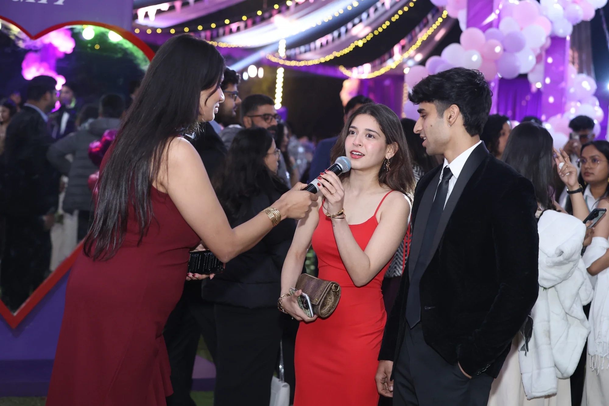 Host interviewing a couple on the prom night floor under string lights and balloons