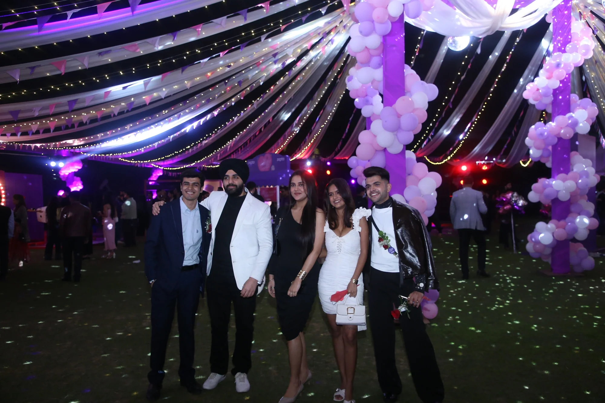 Guests posing together under balloon-wrapped pillars and draped ceiling lights